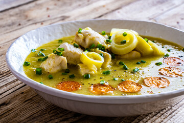 Bowl of hot leek soup with chicken meat on wooden table
