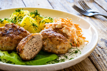 Fried meatballs with boiled potatoes and carrot salad on wooden table
