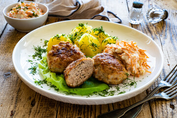 Fried meatballs with boiled potatoes and carrot salad on wooden table
