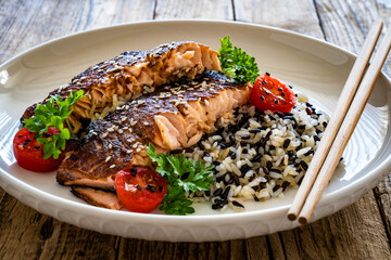 Fried teriyaki salmon steak with black and white rice on wooden table

