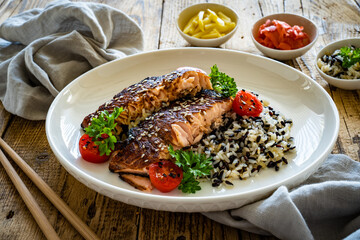 Fried teriyaki salmon steak with black and white rice on wooden table
