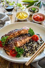 Fried teriyaki salmon steak with black and white rice on wooden table
