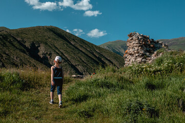 a preschooler girl in a cap walks alone in the mountains along a path, a view from the back. Little...