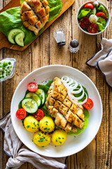 Fried chicken breasts with boiled potatoes and fresh vegetables on wooden table
