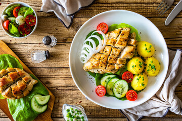 Fried chicken breasts with boiled potatoes and fresh vegetables on wooden table
