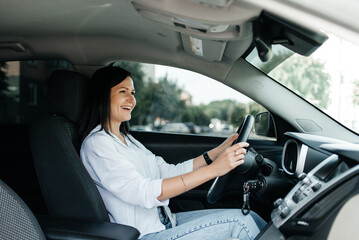 Cheerful young woman in car. Beautiful driver on front seat holding steering wheel.