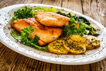 Fried salmon steak with potatoes, spinach and fresh vegetables served on wooden table
