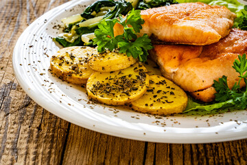 Fried salmon steak with potatoes, spinach and fresh vegetables served on wooden table
