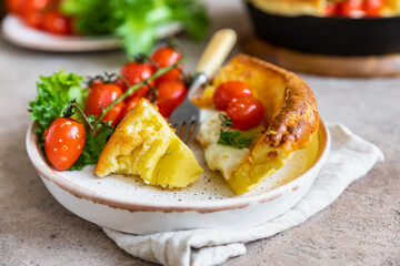 Savory Dutch baby pancake with roasted cherry tomatoes, mozzarella cheese and green salad leaves in serving cast-iron frying pan. Danish cuisine. Hearty breakfast.