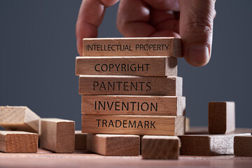man adding a  block showing the words ’Intellectual property’ on top of  other wooden block...