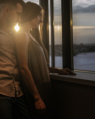 Happy loving couple in hotel standing on window background on sunset