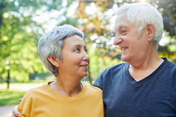 Optimistic attractive elderly 60s couple pose in park
