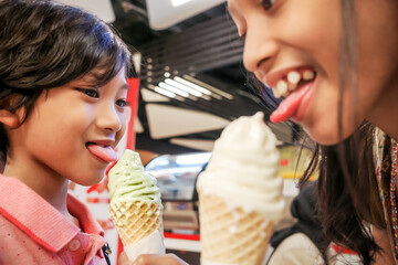 Southeast Asian children, boy and girl enjoy eating green tea and vanilla ice cream together at food court