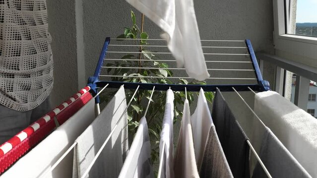 Woman hanging wet clean cloth on laundry drying rack in balkony at home. Close up of female hands hanging washed clothes, towels, linens on clothes wire dryer