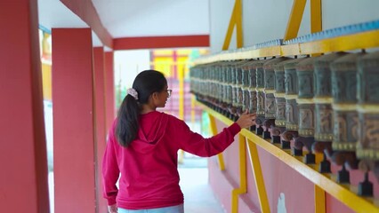 Portrait of Indian girl traveler rotating prayer wheels and speaking mantra of prayer at Himalayan Nyinmapa Tibetan Buddhist Monastery in Manali, Himachal Pradesh, India. Religious background. 