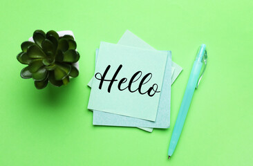 Sticky note with word HELLO, pen and succulent on green background