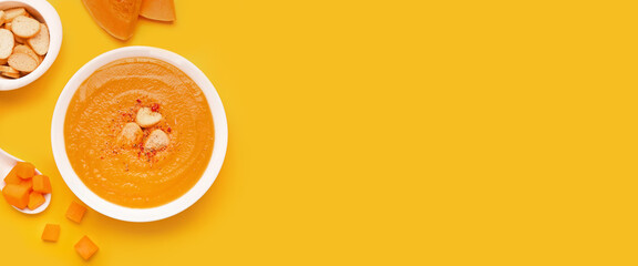 Bowl of delicious pumpkin cream soup and croutons on yellow background with space for text