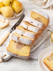 Pear loaf cake sliced on wooden cutting board. Tasty homemade cake baked with whole peeled pears. Seasonal autumn (fall) bakery. Close up view. White wooden table background.