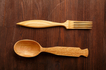 Wooden spoon and fork on a dark brown wooden background.