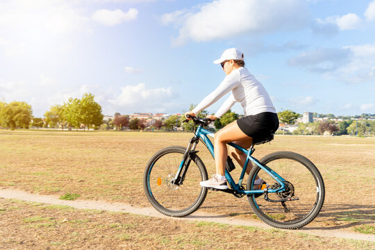 Young woman enjoys a sunny day exercising with her bicycle in the city park. High quality photo