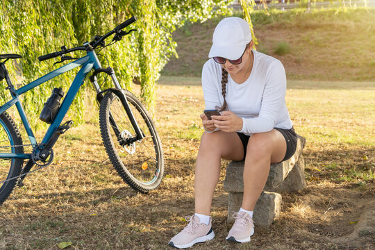 Girl checks her cell phone and rests under a tree next to her bike after exercising. High quality photo