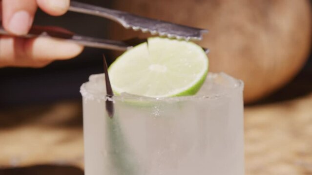 Close up preparation of cocktail tons placing lime on top of clear tropical drink