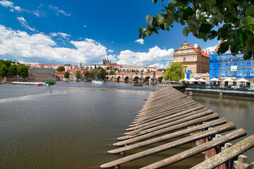 Look over Vltava river to Charles bridge, Prague Castle in background under blus sky with white...