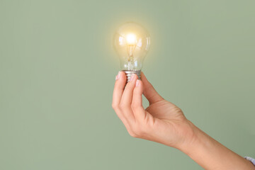 Female hand with glowing light bulb on green background