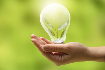 Female hand holding light bulb with plant inside on green background. Ecology concept
