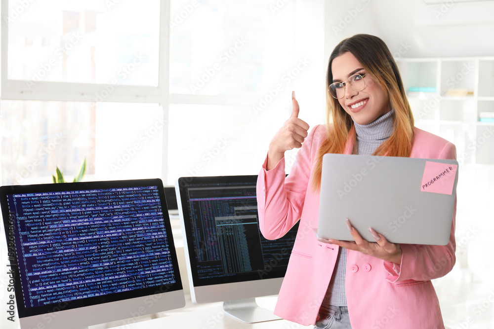 Poster transgender programmer with laptop showing thumb-up in office