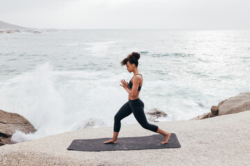 Fototapeta na wymiar Side view of young female in fitness wear practicing yoga on mat by seaside