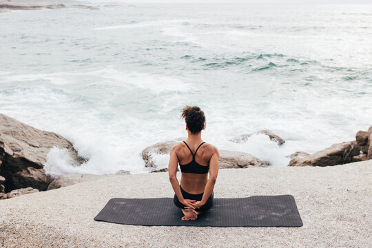 Woman sitting on mat by ocean warming up hands