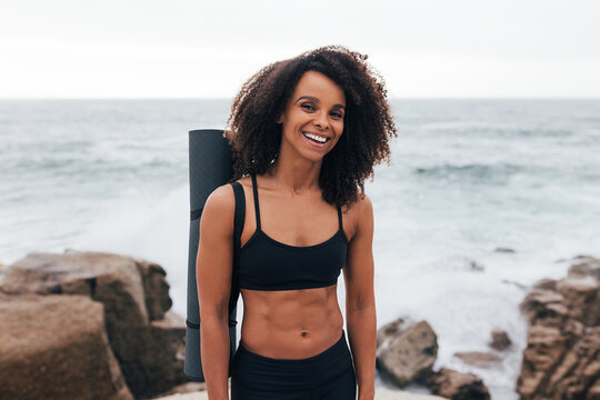 Portrait of a laughing woman with curly hair wearing fitness clothes with yoga mat