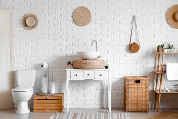 Interior of cozy bathroom with sink, toilet bowl and laundry basket