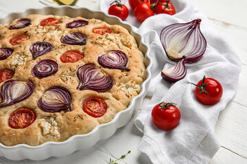 Baking dish with tasty Italian focaccia and vegetables on light wooden table, closeup