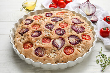Baking dish with tasty Italian focaccia on light wooden table, closeup