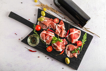 Wooden board with delicious jamon and bowl of oil on light background