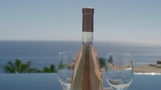 Close up of pink rose bottle and wine glasses with pool and ocean view in Cabo, Baja Sur, Mexico on sunny day