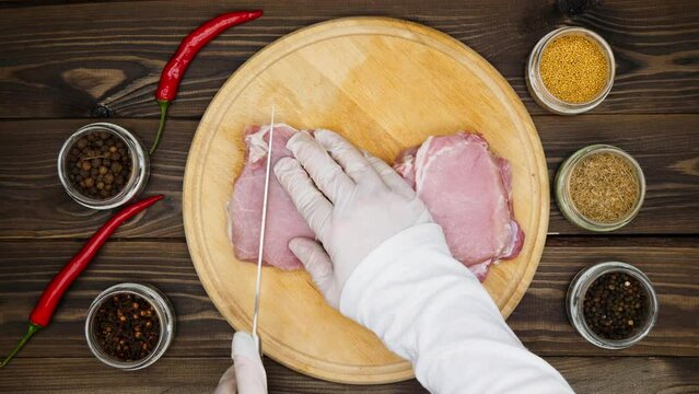 Slicing meat. Hands cut meat steaks on a cutting board on a wooden table into slices for marinating with a large knife. Meat preparation. Red hot chili peppers, cumin, mustard. Close-up. Top view