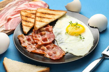 Plate of tasty fried egg, bacon and toasts on blue background, closeup