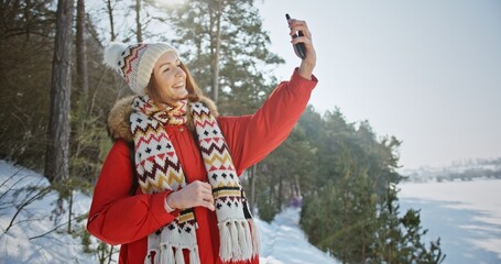 A young girl in the winter forest calls to a web conference on a tourist sunny day