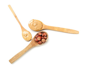 Wooden spoons with tasty hazelnut butter and nuts on white background