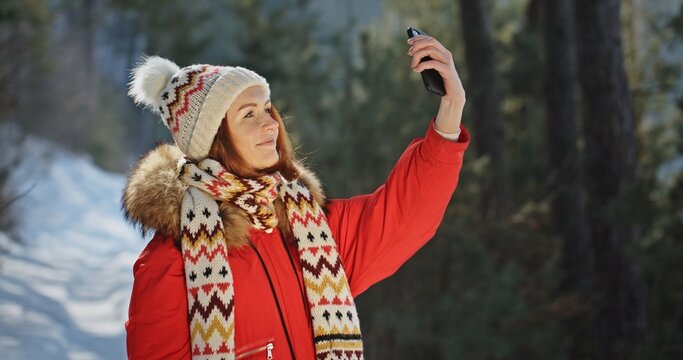 Young woman in stylish scarf takes selfies in winter forest