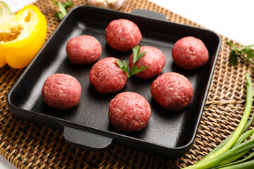 Wicker mat with baking dish, raw meat balls and vegetables on white background