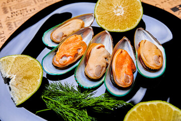 mussels on a black dish with a slice of lemon and a bunch of dill