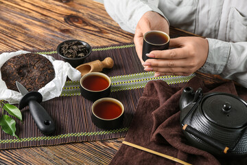 Woman with cup of puer tea at wooden table, closeup