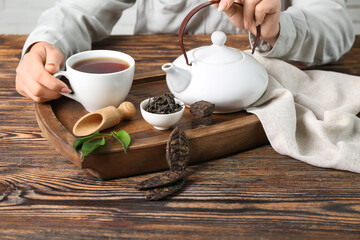 Woman with pot and cup of puer tea at wooden table, closeup