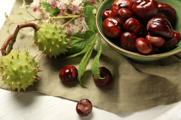 Bowl with fresh chestnuts on light wooden table, closeup