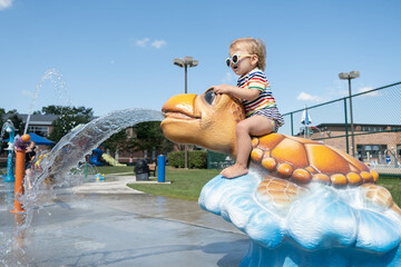 Toddler sits high on a turtle spraying water at a splash pad