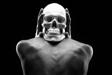 A thin woman sits with her back turned and holds a human skull in her hands.On a black background. One of the halloween symbols